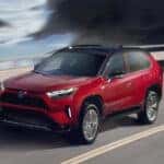 A red 2024 Toyota RAV4 Prime driving near an ocean.