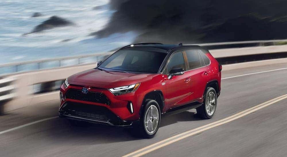A red 2024 Toyota RAV4 Prime driving near an ocean.