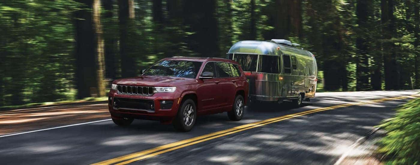 Red 2022 Jeep Grand Cherokee WL towing a trailer through a forest.