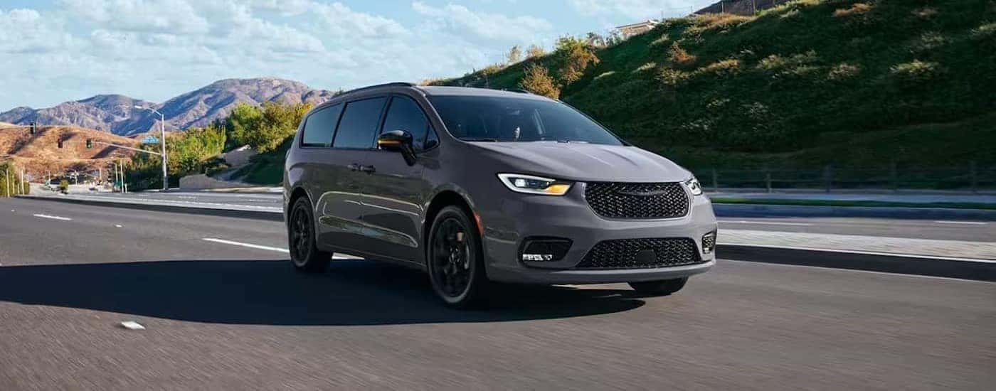 Grey 2024 Chrysler Pacifica driving down a road.