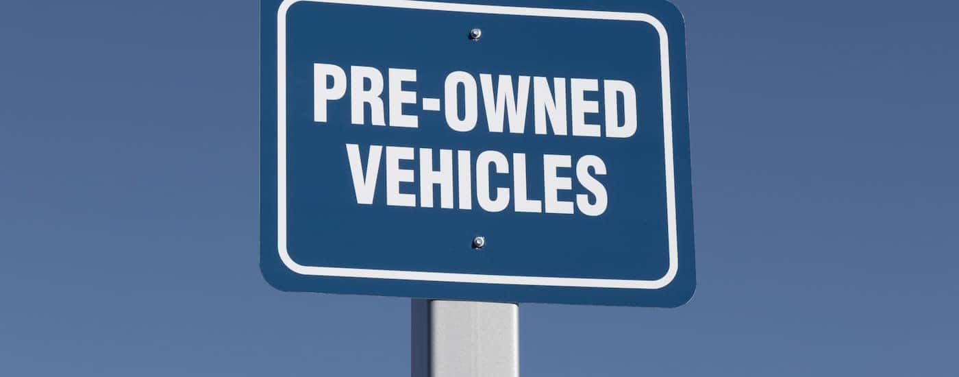 A blue sign says 'Pre-Owned Vehicles,' is shown on the lot of a Certified Pre-Owned car dealer.