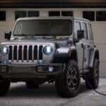 A silver 2024 Jeep Wrangler 4x3 charging in a driveway