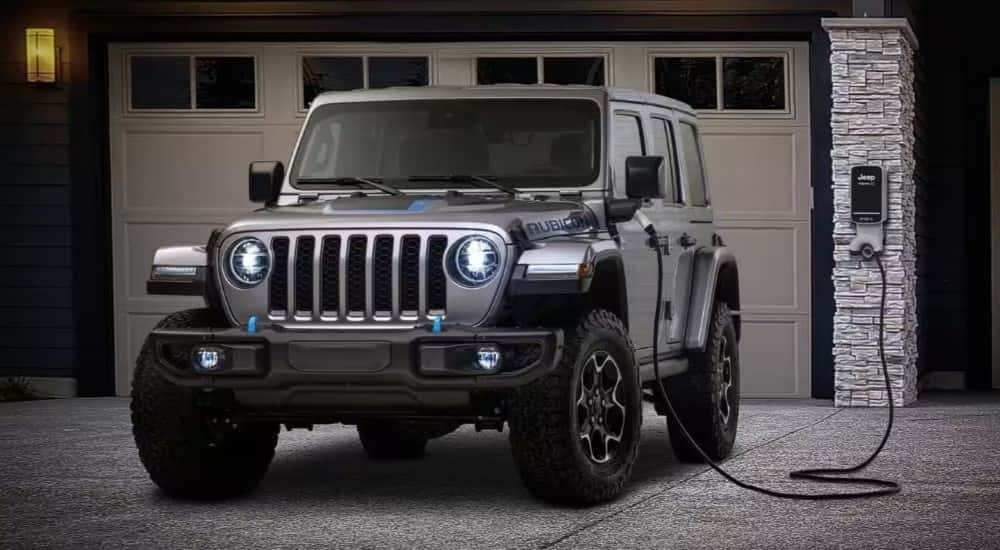 A silver 2024 Jeep Wrangler 4x3 charging in a driveway