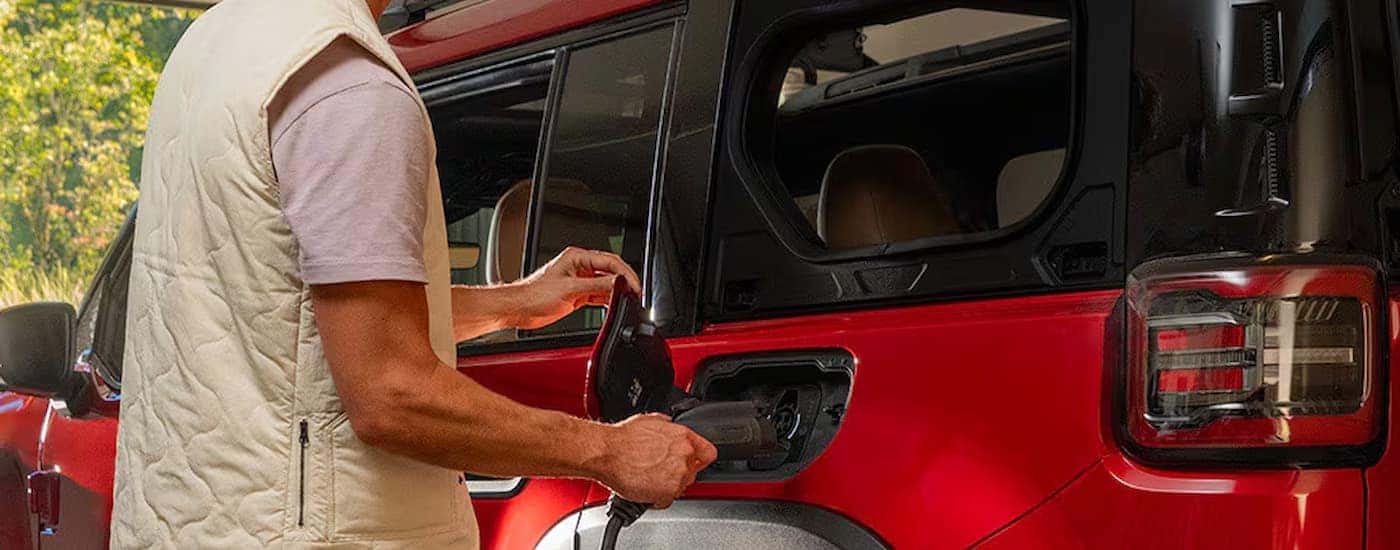 Man charging a red 2026 Jeep Recon in a garage