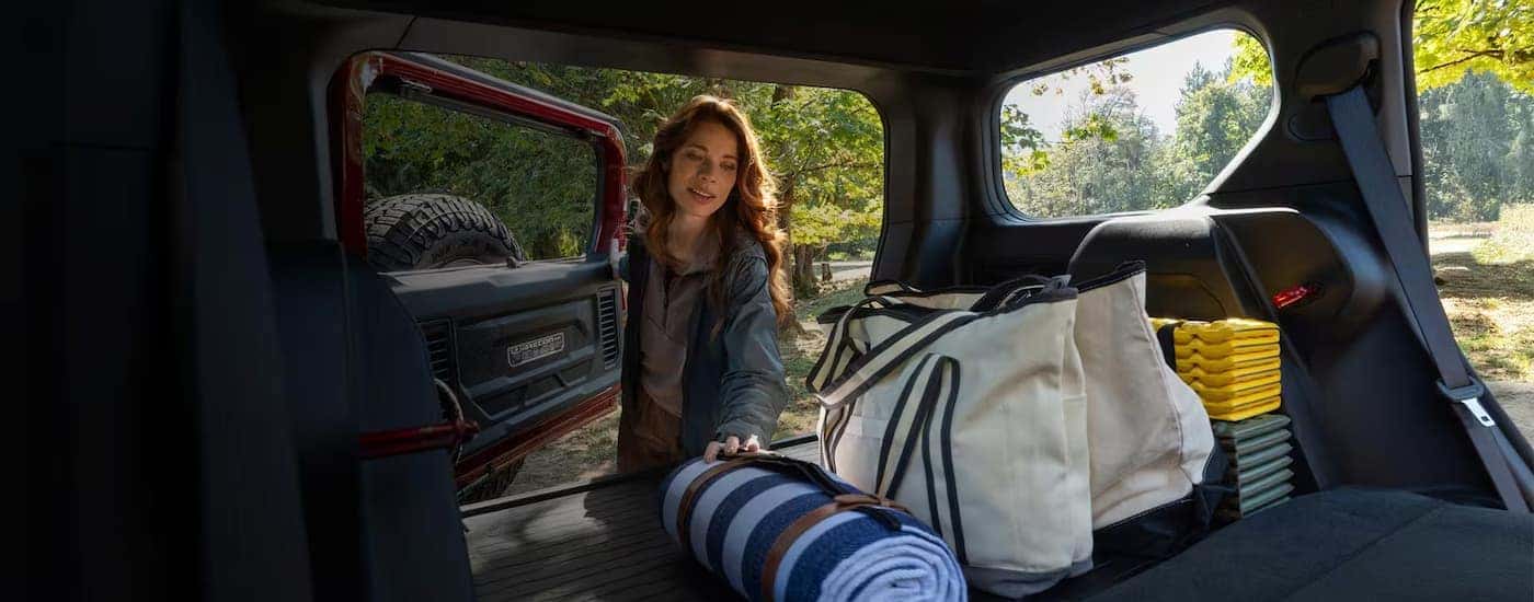 Woman grabbing picnic gear from the back of a red 2026 Jeep Recon