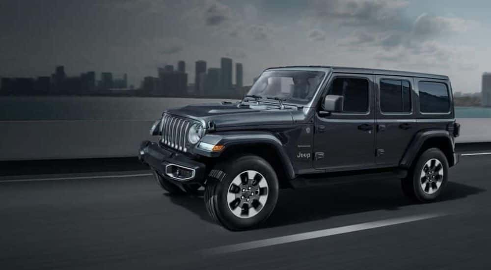 A gray 2018 Jeep Wrangler Sahara Unlimited driving near a city.